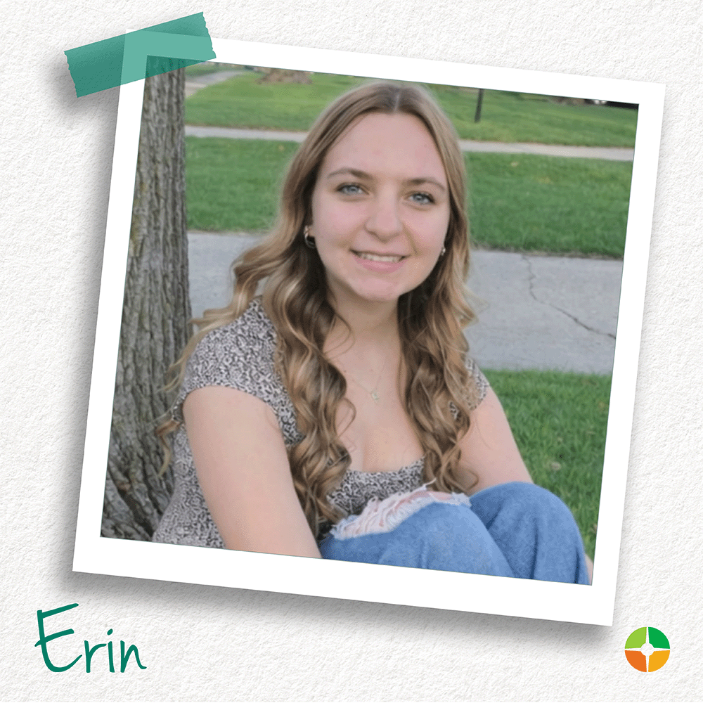 Polaroid-style photo of a smiling young woman with long wavy hair sitting outdoors near a tree. She wears a patterned top and jeans. The name “Erin” appears in green script at the bottom, with a small logo in the corner.
