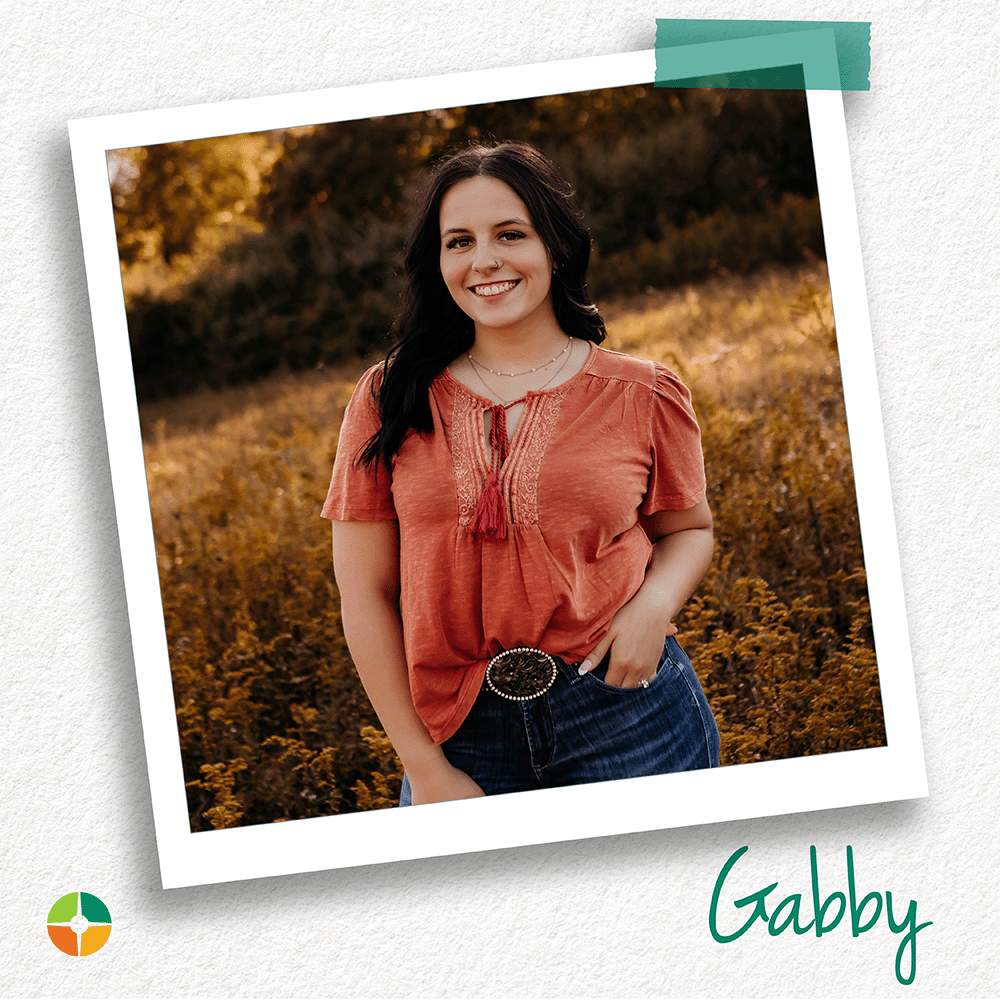 A young woman smiles while standing in a sunlit field surrounded by warm autumn colors. Wearing a rust-colored blouse and jeans, she poses confidently with a relaxed expression, creating a welcoming and natural outdoor portrait. A young woman smiles while standing in a sunlit field surrounded by warm autumn colors. Wearing a rust-colored blouse and jeans, she poses confidently with a relaxed expression, creating a welcoming and natural outdoor portrait.