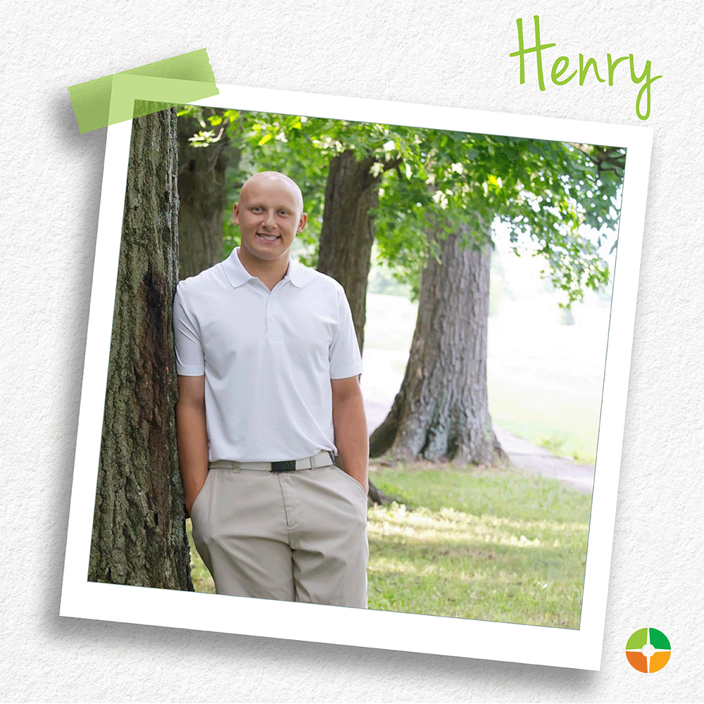 Polaroid-style photo of a smiling young man standing outdoors beside a tree in a grassy area. He wears a white polo shirt and khaki pants. The name “Henry” appears in green script at the top, with a small logo in the corner.