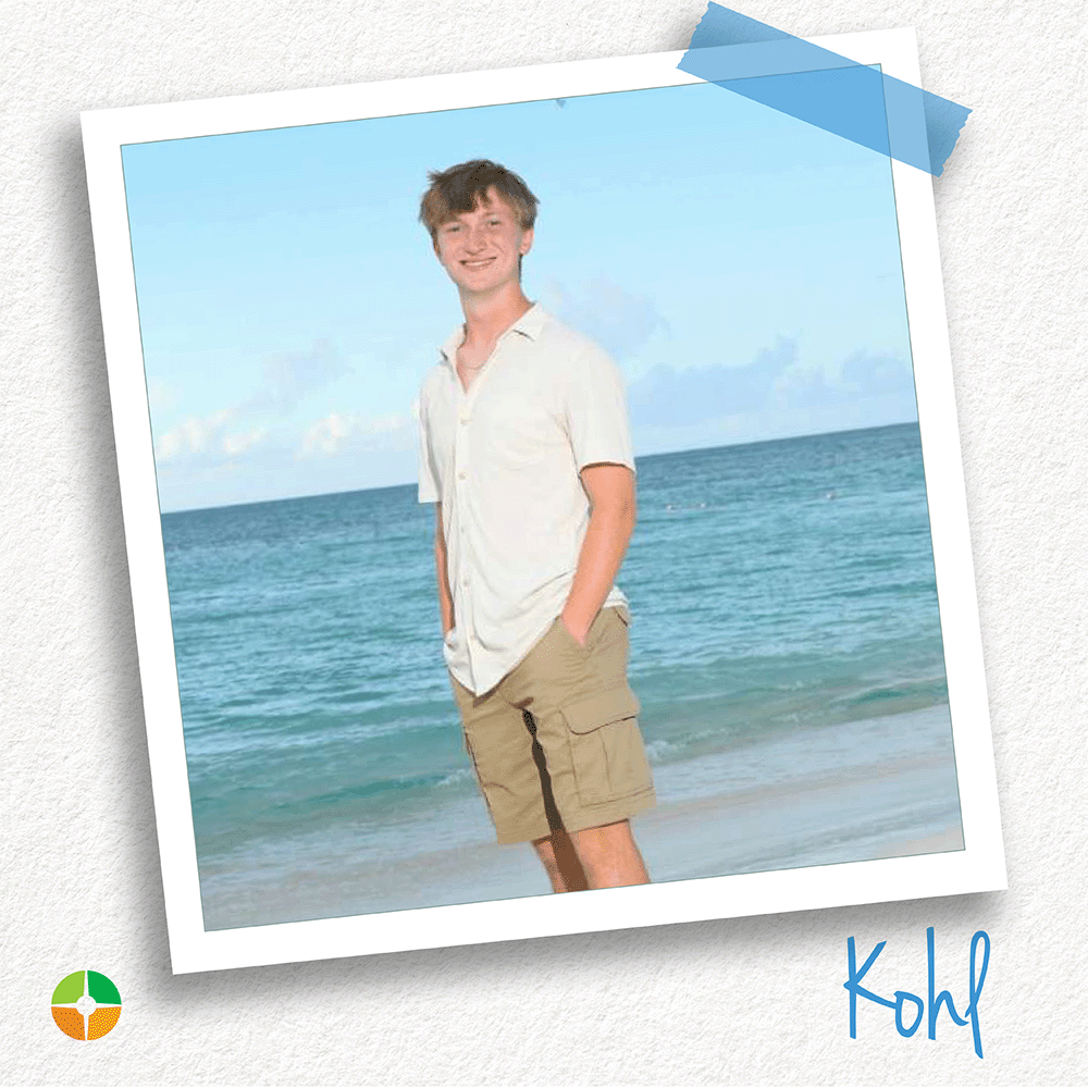 A young man stands along a sandy shoreline with the ocean stretching behind him. Wearing a light button-down shirt and cargo shorts, he smiles casually at the camera with his hands in his pockets. The bright beach setting creates a relaxed and confident portrait. A young man stands along a sandy shoreline with the ocean stretching behind him. Wearing a light button-down shirt and cargo shorts, he smiles casually at the camera with his hands in his pockets. The bright beach setting creates a relaxed and confident portrait.
