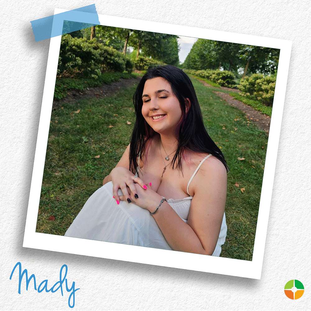 A senior portrait-style photo of Mady seated on a grassy path surrounded by trees and greenery. She is smiling while wearing a light-colored dress, creating a relaxed and natural outdoor setting. A senior portrait-style photo of Mady seated on a grassy path surrounded by trees and greenery. She is smiling while wearing a light-colored dress, creating a relaxed and natural outdoor setting.